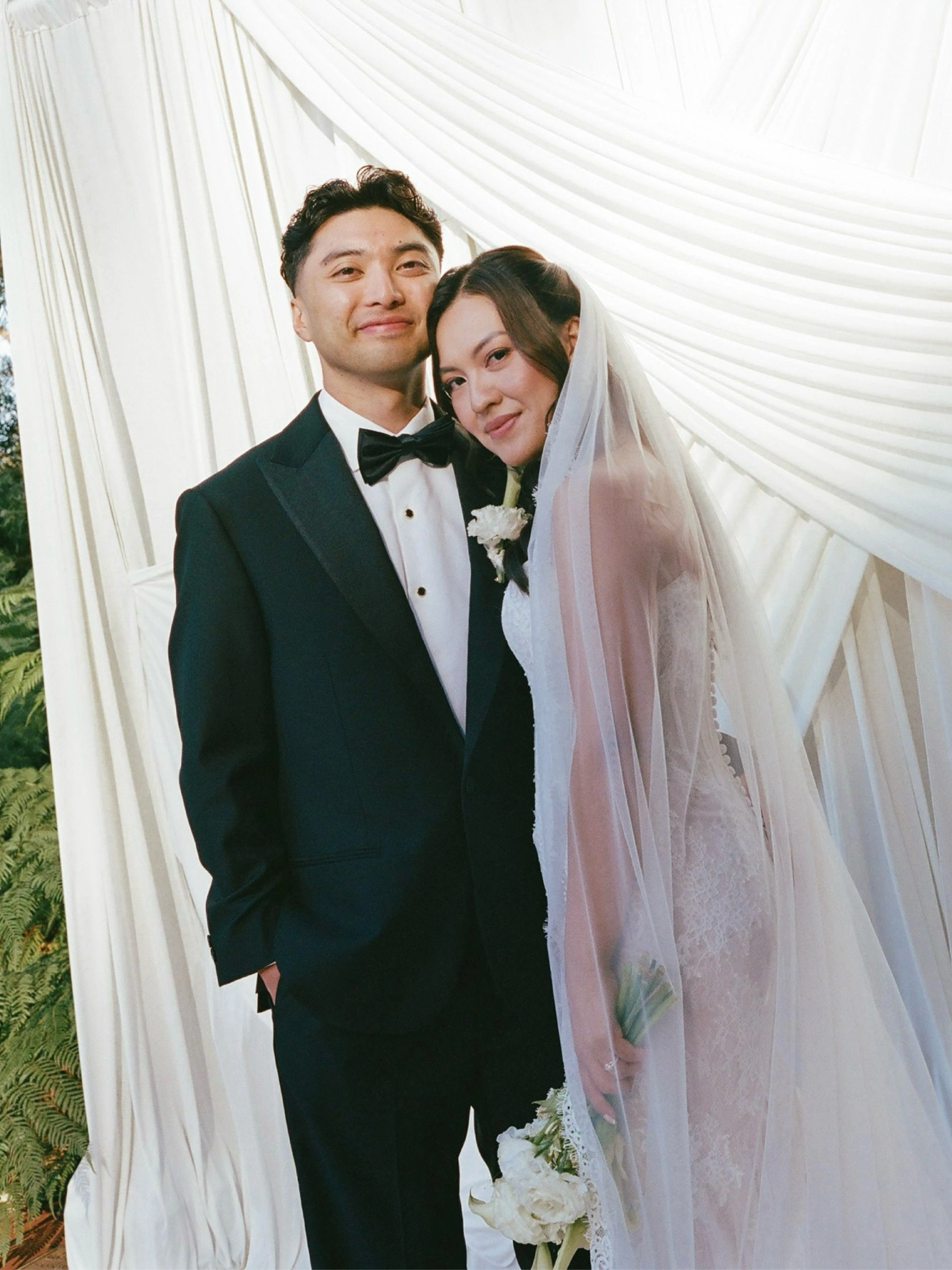 Bride in a veil and groom beneath soft white drapery